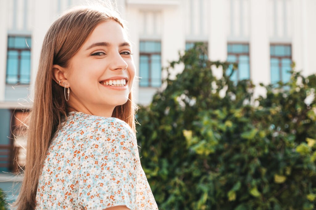 Portrait of young beautiful smiling hipster woman in trendy summer dress. Sexy carefree woman posing on the street background at sunset. Positive model outdoors. Cheerful and happy